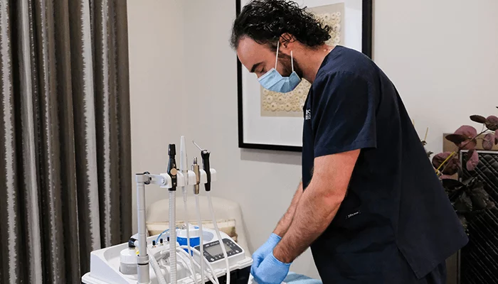 Dental professional in PPE working beside a mobile dental equipment cart in a clinical setting