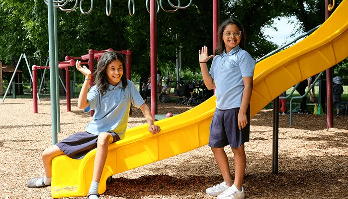 Two school children in uniforms waving happily at a playground