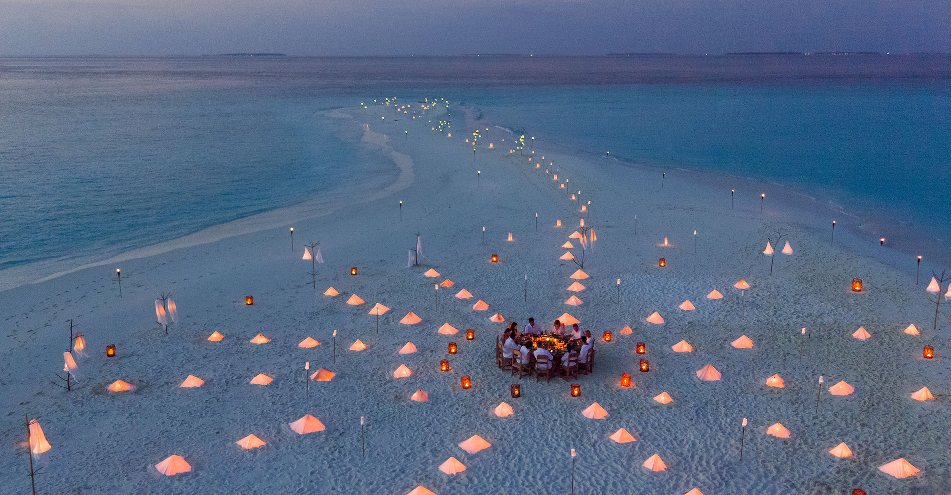 Aerial view of private sandbank dinner with lanterns on a Maldives sandbar at twilight