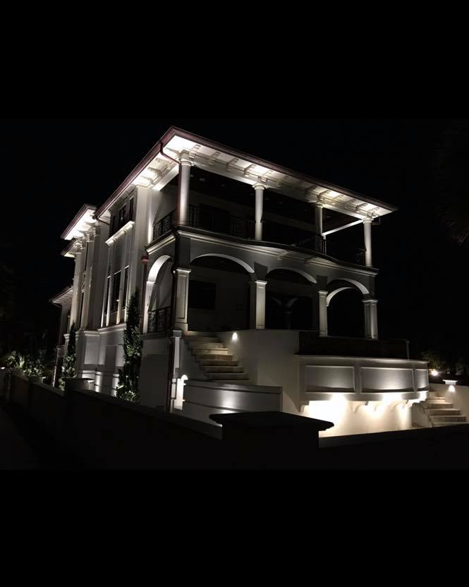 Dramatic nighttime exterior of a neoclassical mansion with architectural uplighting illuminating tall columns and arched verandas