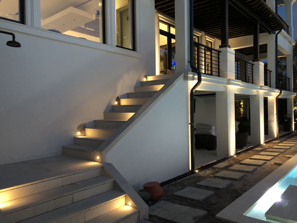 Modern two-story home exterior with step lighting, column accents, and poolside walkway illumination