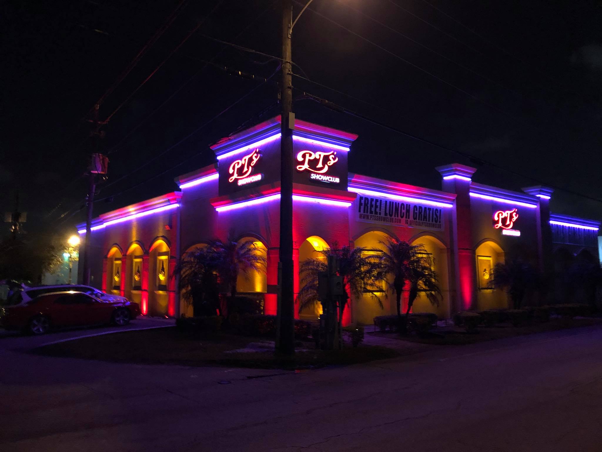 Commercial entertainment venue illuminated at night with neon lights and palm trees along the exterior facade