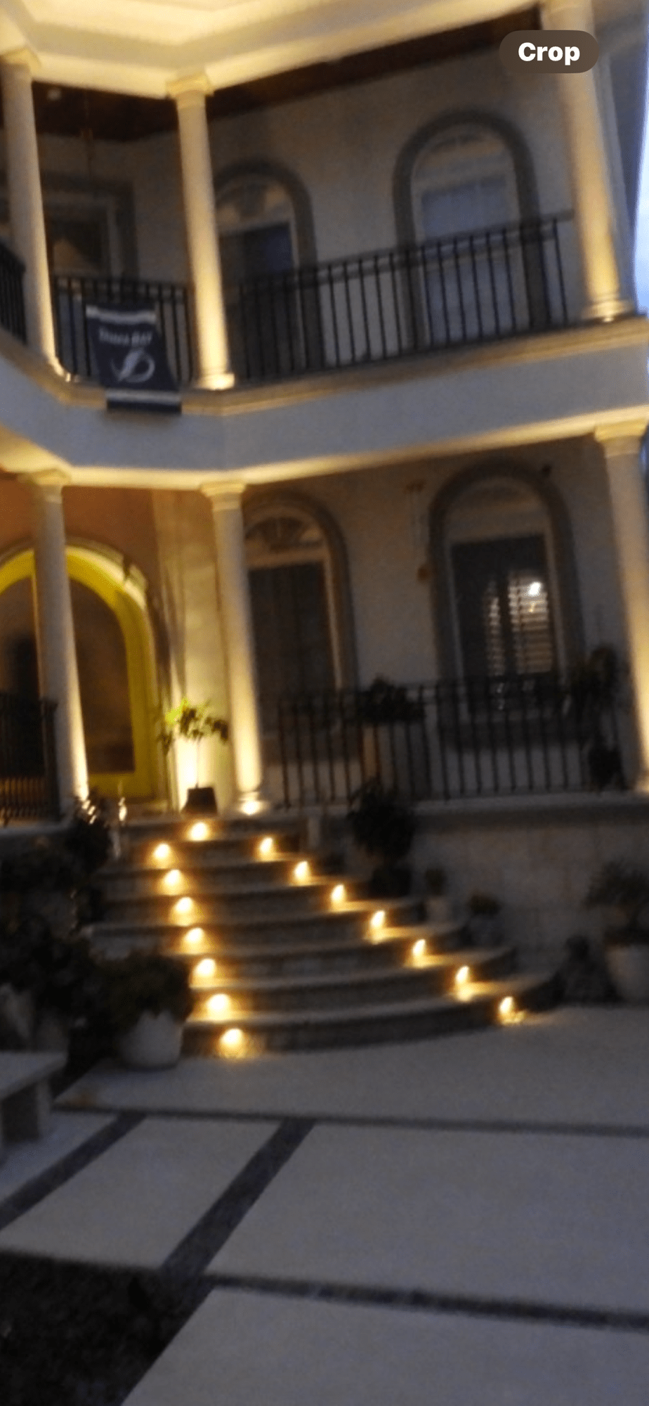 Nighttime exterior of an upscale building with warm uplighting illuminating white columns and an arched entryway with step lights