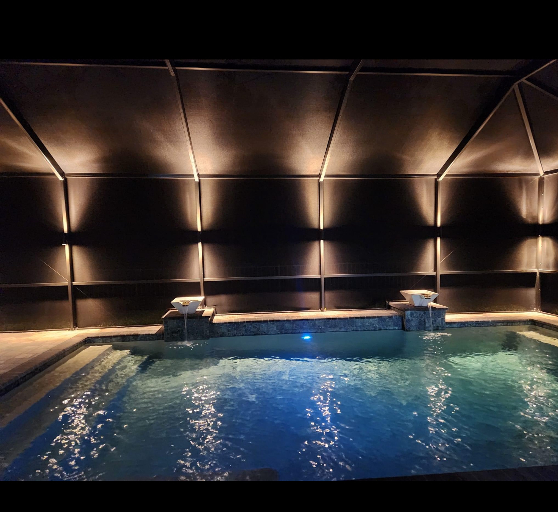 Indoor swimming pool inside a screened enclosure at night with dramatic accent lighting and teal water reflections